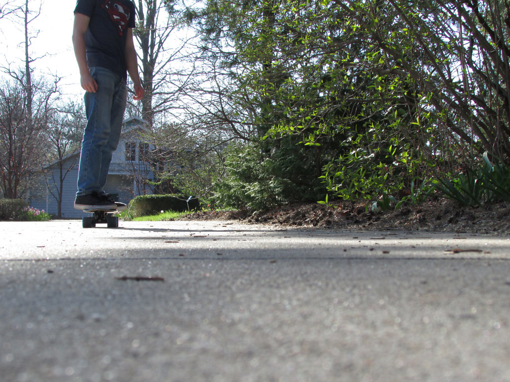 Young man skateboarding on a sidewalk in late spring
